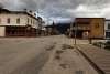 Empty asphalt streets and wooden boardwalk with false front, 1800's Gold Rush style buildings lining each side under cloudy skies and powerlines.