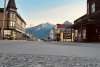 aggregate asphalt in the foregroud gives rise to gold rush era false front buildings on either side of a virtually empty Broadway street with massive snow topped mountains in the background a blue skies at dusk