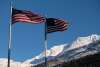 Two American Flags blowing in the wind with clear blue skies and snow capped mountains in the background in front of the border crossing station looking to the East.