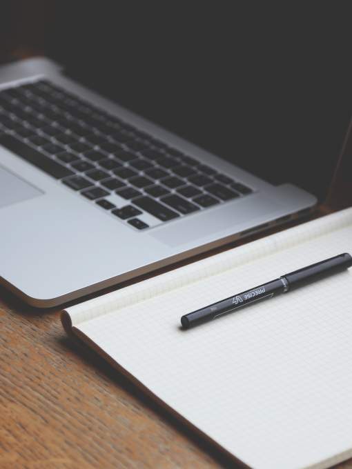 Laptop computer with notebook and pen laying beside it