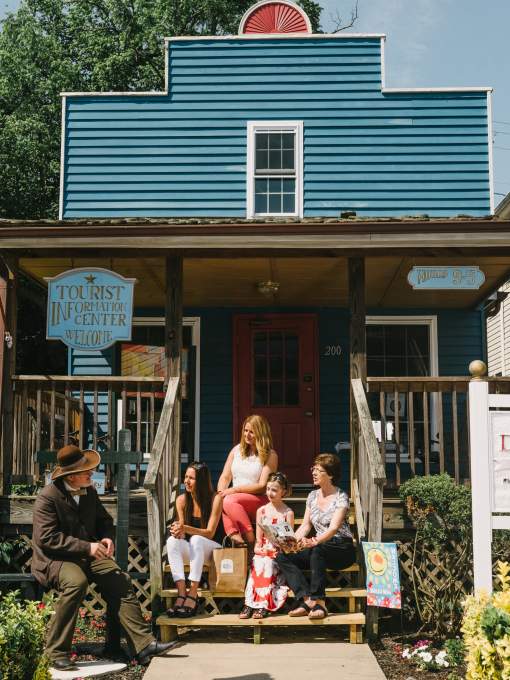 A history volunteer sitting on a bench talking with women sitting on the stairs of a tourist information center