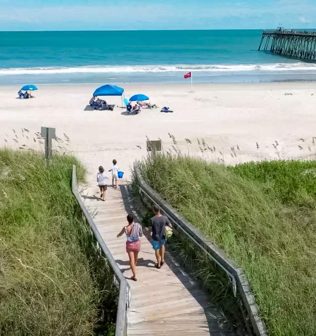A family walking to the sand by the pier on Kure Beach.