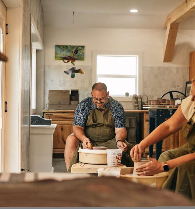Two people sitting, making pottery together in a studio space.