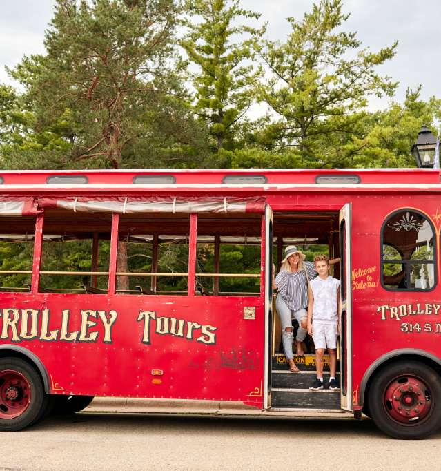 A woman and child standing in front of a red trolley bus.