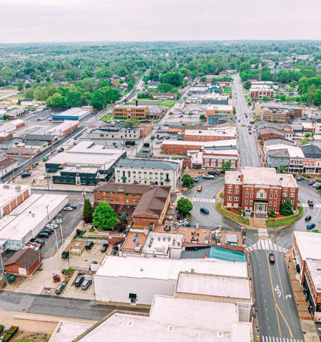 An aerial view of downtown Elizabethtown, KY, showcasing the layout of streets, buildings, and greenery, under an overcast sky.