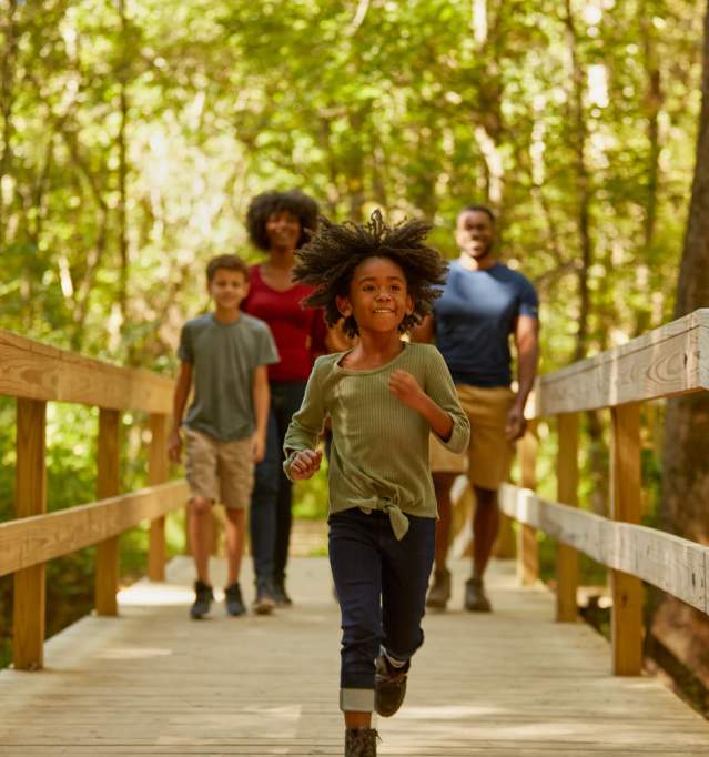 a family walking on a bridge with a little girl running toward the camera