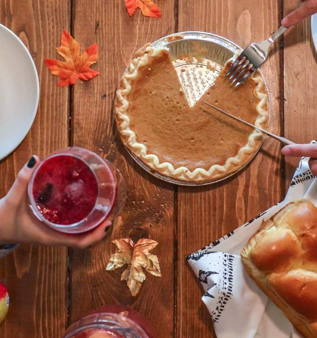 A Thanksgiving table with pumpkin pie, bread and a holiday cocktail.