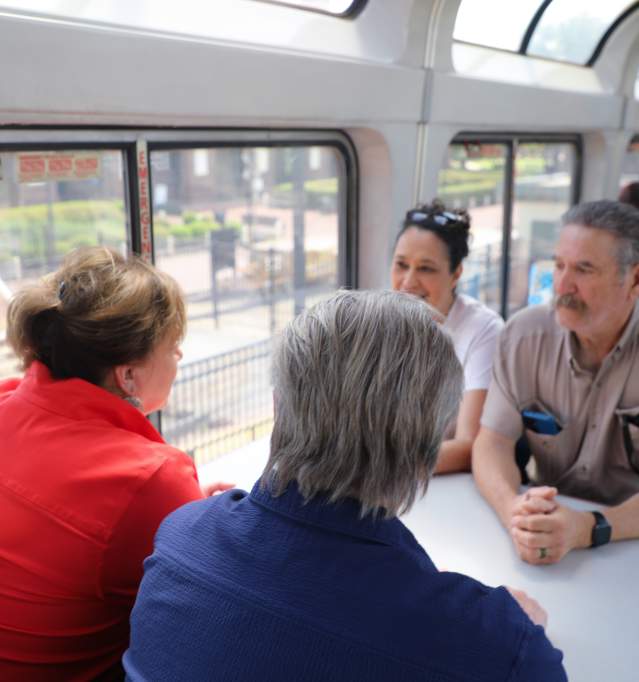 Group of four people - two men and two women talking and sitting down at a table in the observation cart of the Amtrak Texas Eagle train. Outside the window is the Santa Fe Depot.