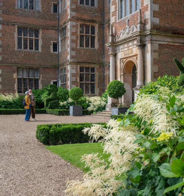 a couple walking along a path outside Doddington Hall in the sun