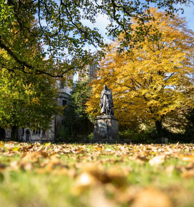 Alfred Tennyson statue surrounded by autumnal trees outside Lincoln Cathedral with blue skies