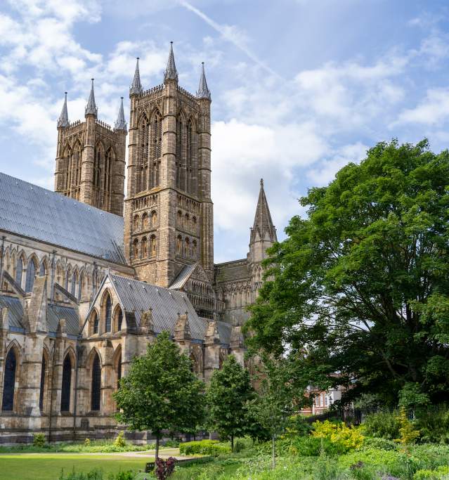 exterior of Lincoln Cathedral towers under blue skies with trees in foreground