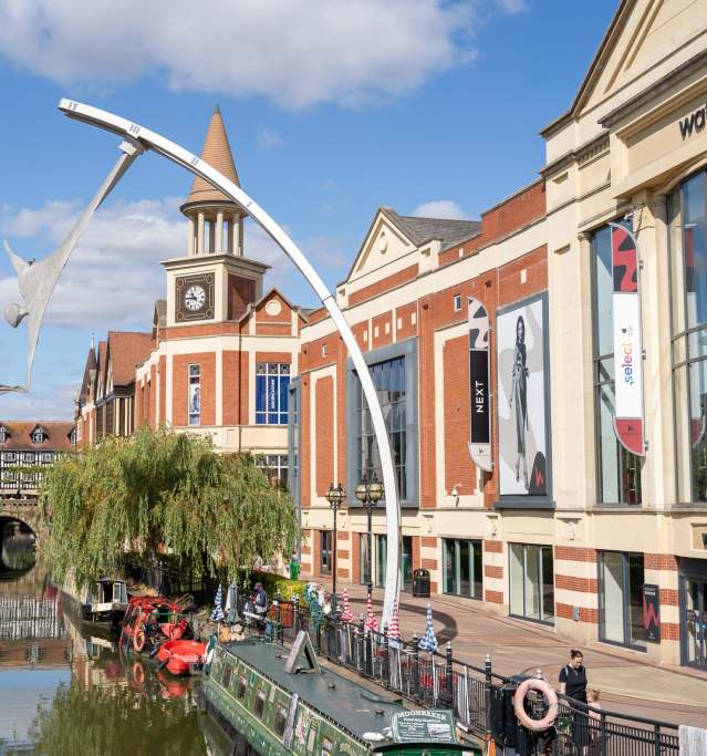 Canal boats on the river through Lincoln with a sculpture of two people touching hands, with waterside shopping centre in the background