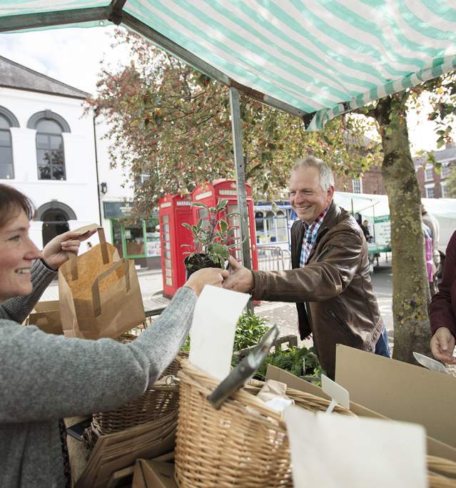 a man and woman stood at a market stall purchasing fruit and vegetables