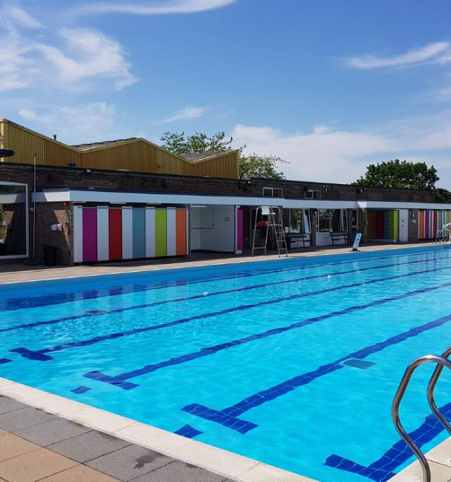 An outdoor swimming pool with changing facilities in background