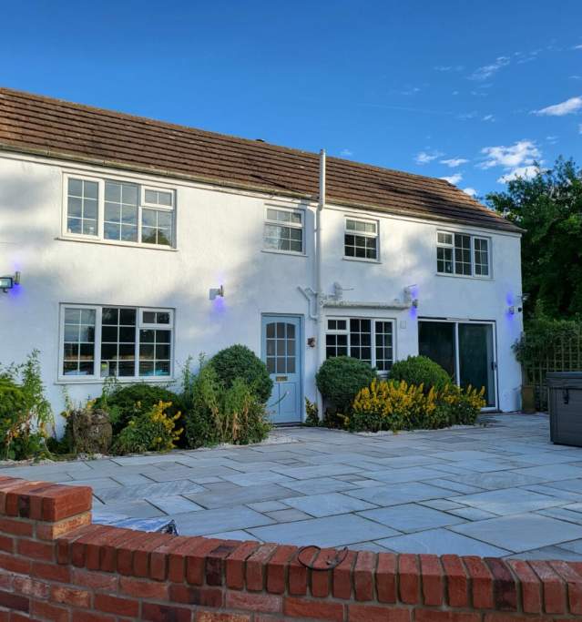 a white cottage from outside with brick wall surrounded by bushes