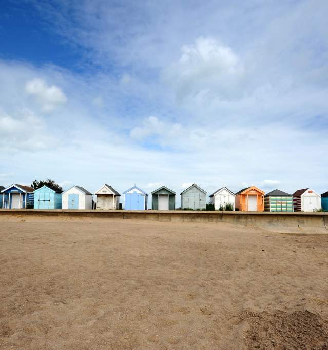 a line of beach huts with sand and blue skies