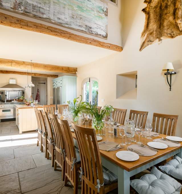 A dining table in a farm cottage with beamed roof and sunlight shining through doorway