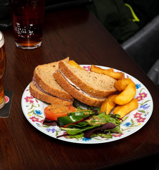 a beer and a sandwich on a plate in a pub with chips