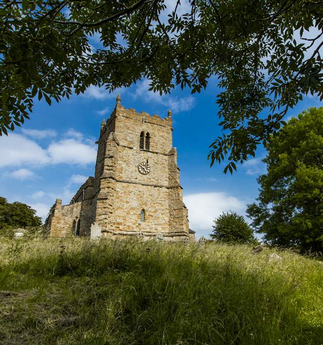 a church on a hill surrounded by trees and grass under blue skies