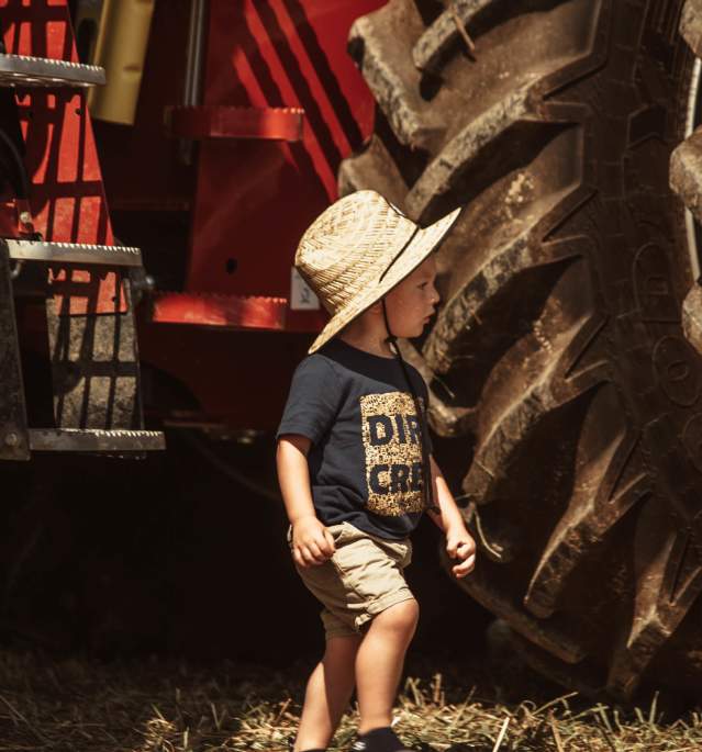 Young boy with hat walking past tractor wheels