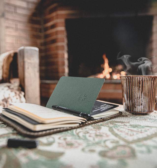Book and cup of steaming coffee in front of fireplace