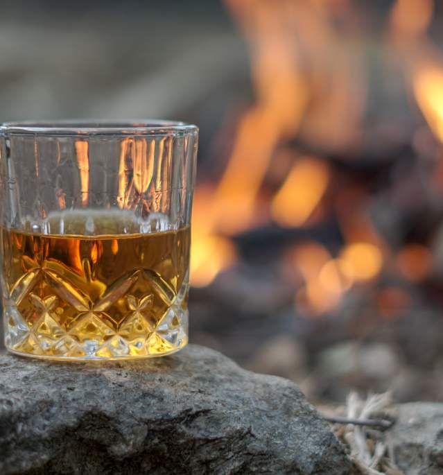 Glass of dark liquor sitting by outdoor firepit
