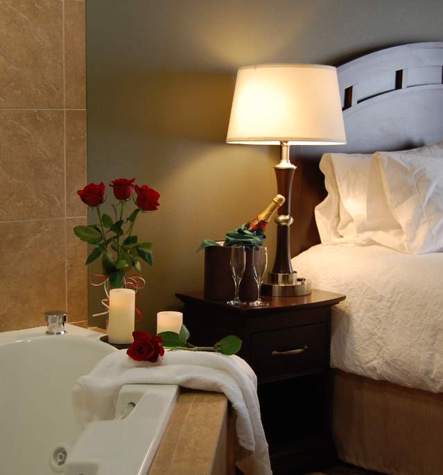 Room with bed and vase of red roses on bathtub