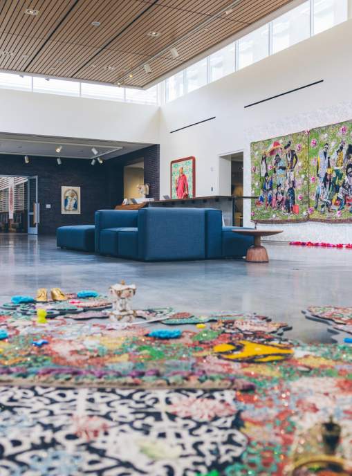 A spacious art gallery featuring vibrant wall murals and colorful floor installations. Modern seating is visible, enhancing the creative atmosphere.