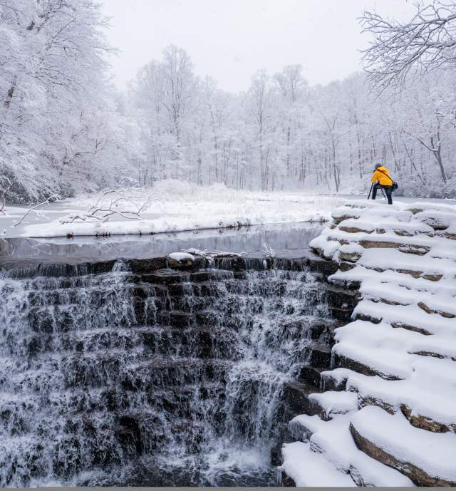 Man taking a picture with a camera on a snow covered waterfall in the Laurel Highlands