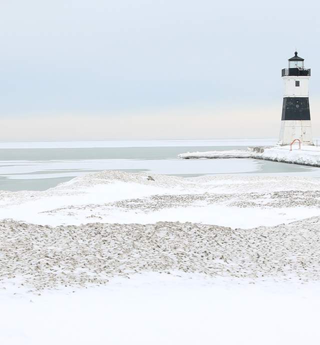 A light house sitting on a dock with snow and ice covering Lake Erie