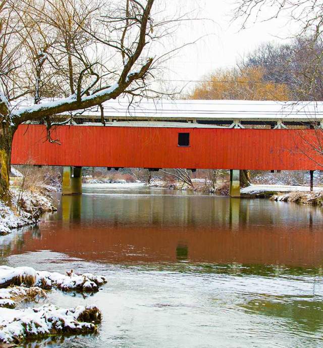 A red covered bridge over a river in the Lehigh Valley with snow on the ground