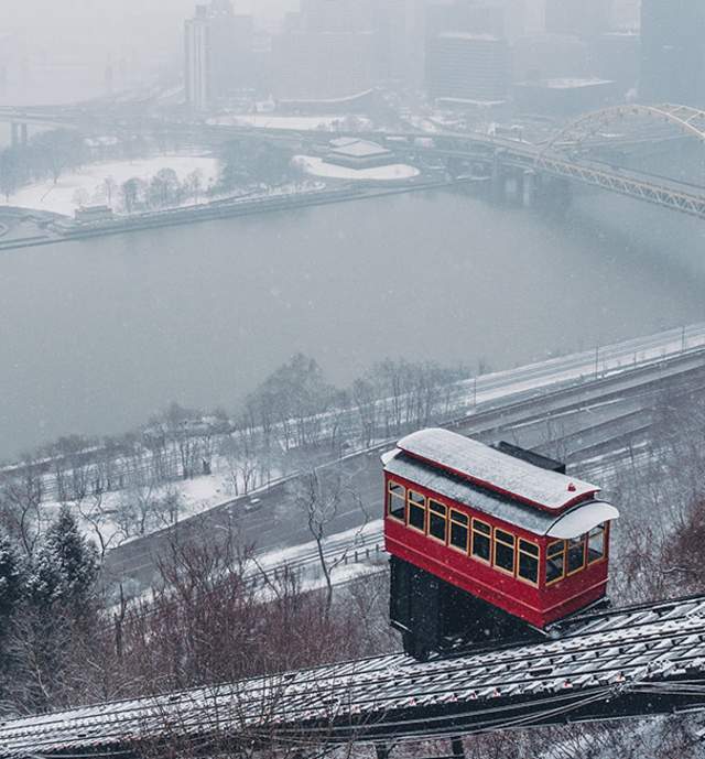 A red trolley car on the side of a hill making its way down the tracks with snow surrounding it
