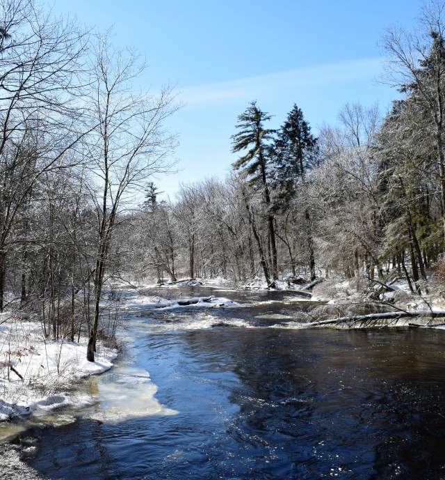 A river flowing in a wooded area in the Pocono Mountains in winter with snow on the ground