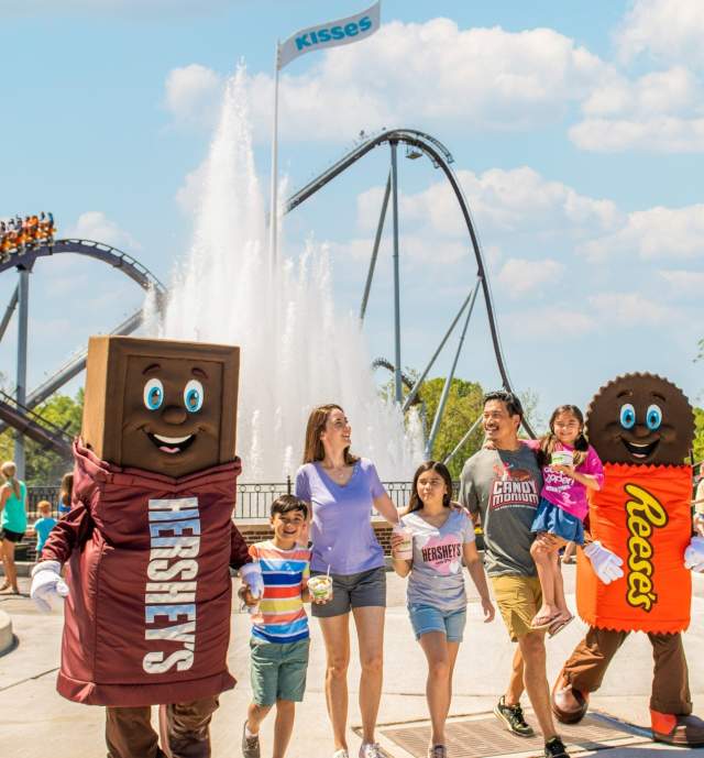 A family of five walking with two mascots in an amusement park