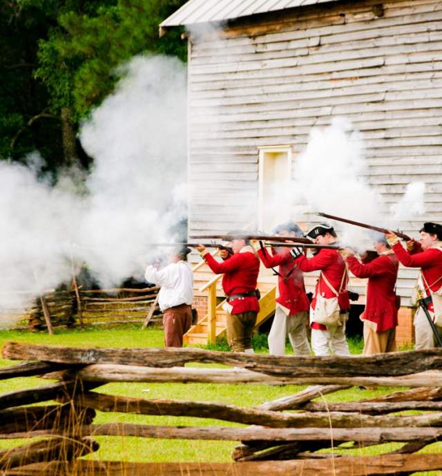 A live reenactment of a war with a wooden building in the background