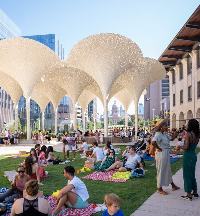 Groups of people standing around and sitting on picnic blankets across the Blanton Museum's lawn, in between museum buildings.