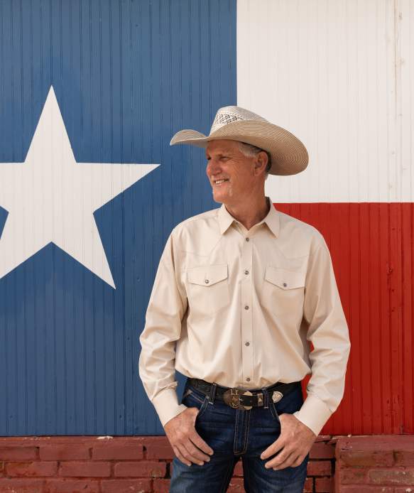 Man wearing a cowboy hat in front of Texas flag mural