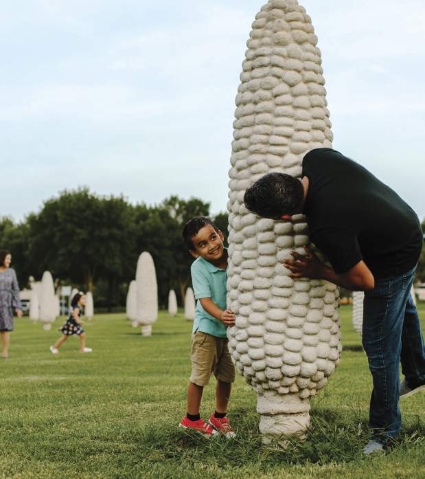 A father and son hiding behind a concrete ear of corn at the Field of Corn public art installation.