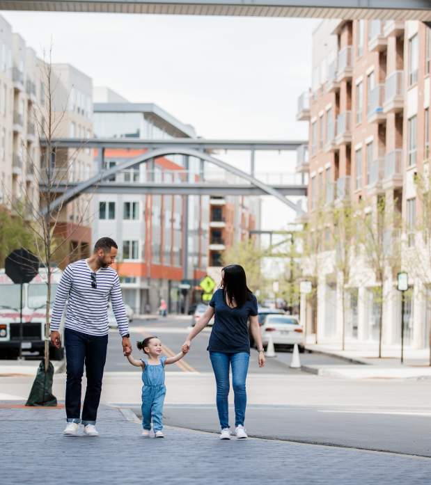 A mom and dad holding handing with their daughter between them in the streets of Bridge Park