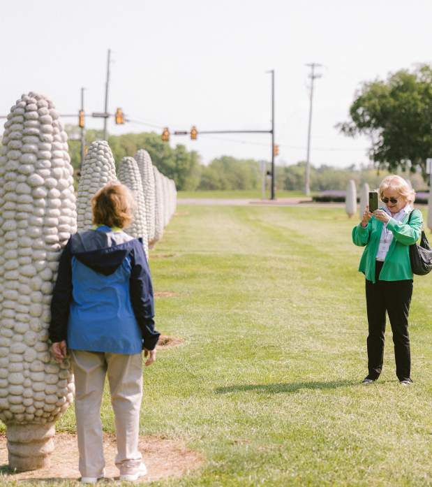 Woman takes a photo of another woman posing beside an oversized concrete corn sculpture at Dublin’s Field of Corn.