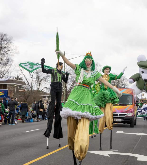 A group of stilt walkers dressed in green performing down the street in the St. Patrick's Day Parade.