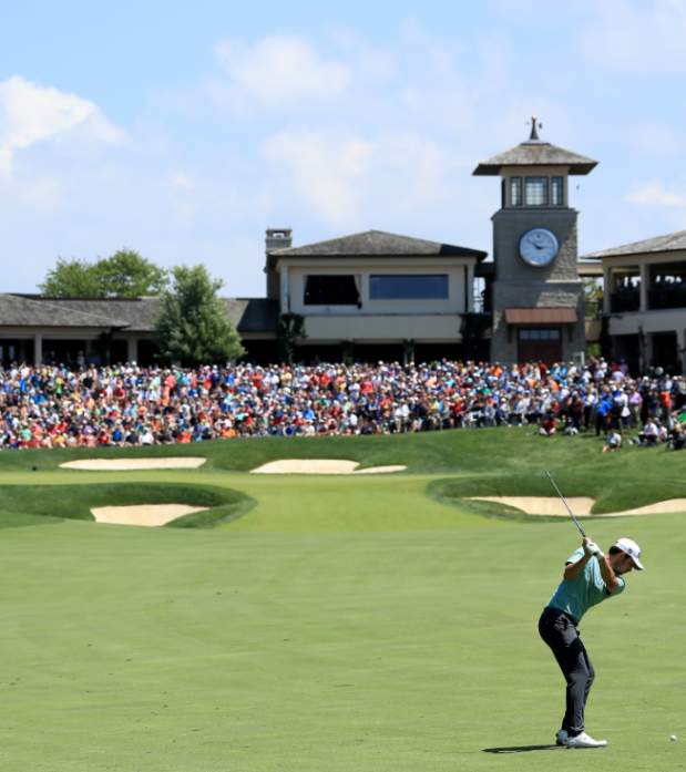 Golfer swining club at golf ball towards the 18th green that is surrounded by a crowd at the Memorial Touranemnt.