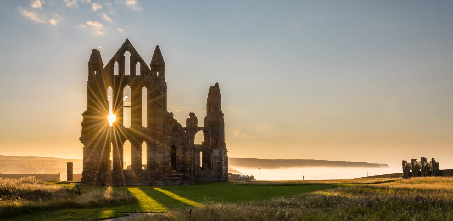 Whitby abbey at dusk, the sun peeking through an arched window