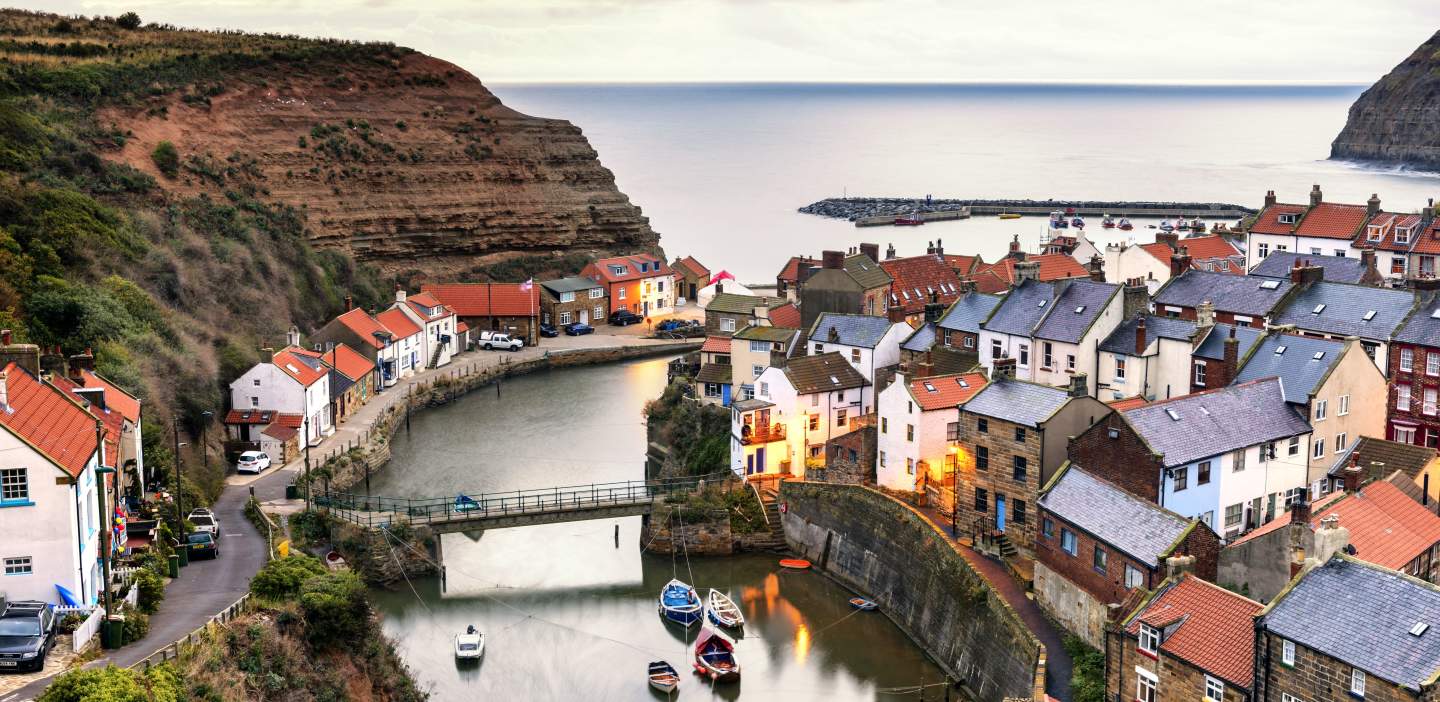 The multi-coloured terraced roofs of Staithes cling to the beck on a calm day