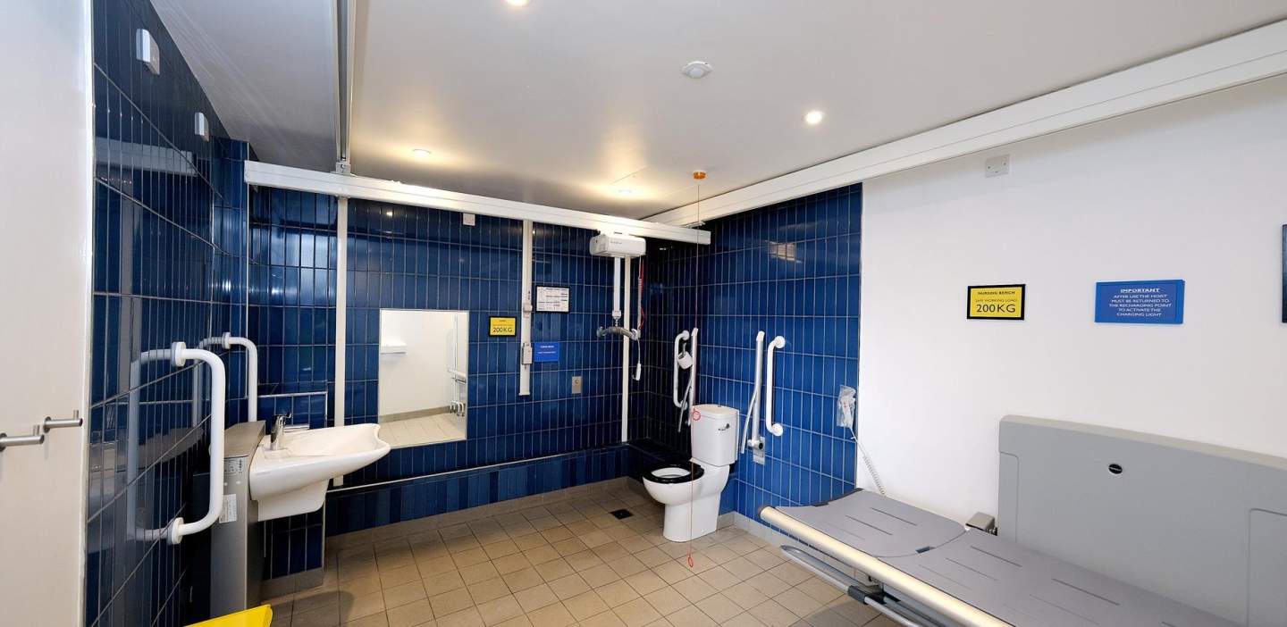 A clean, dark-blue tiled bathroom with baby-changing facilities and accessibility aids around the loo