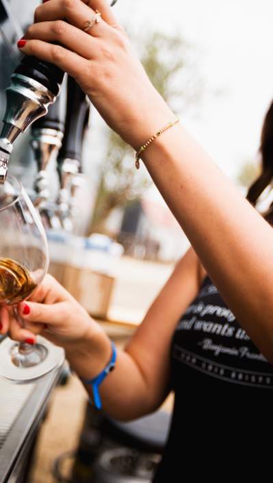 A woman pouring beer from a tap into a glass at SLO Cal bar