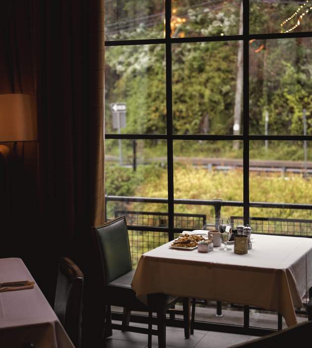 An empty chair in front of a set table at a restaurant in front of a large window