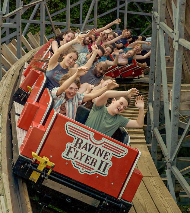 People riding a wooden roller coaster with the arms in the air