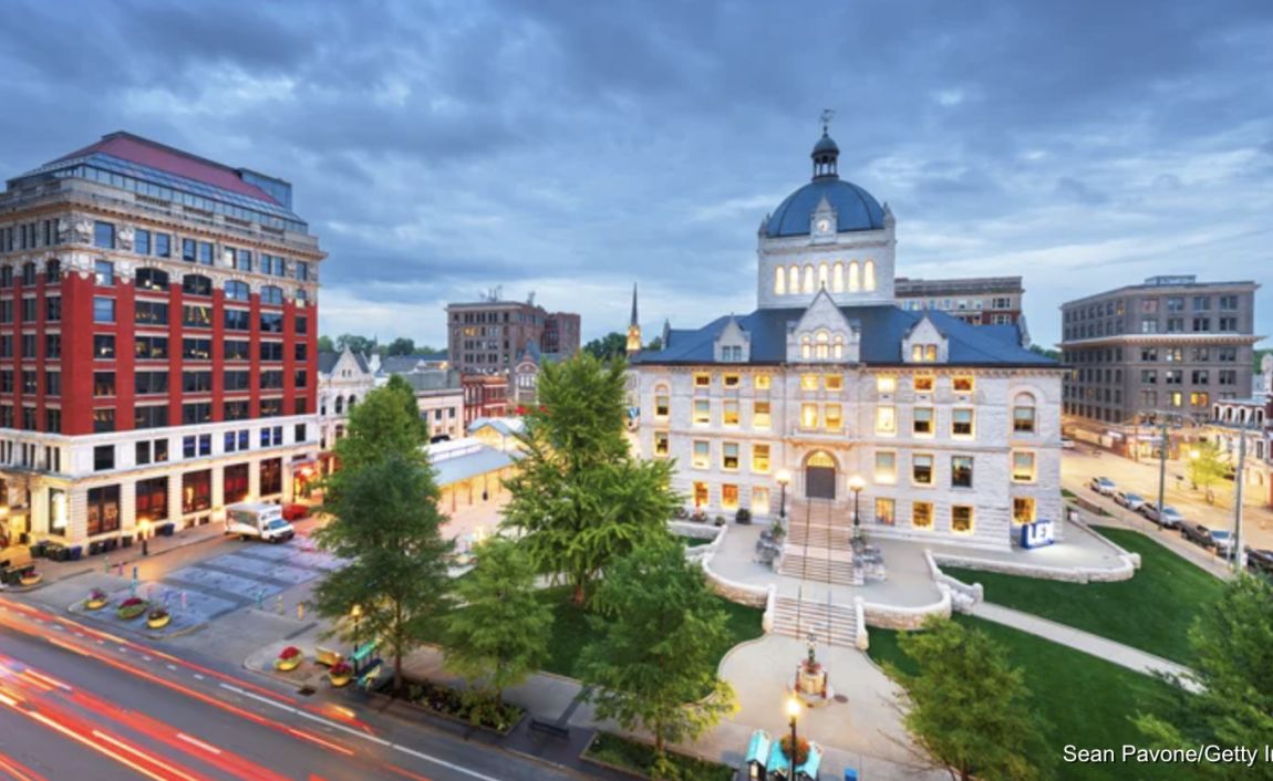 Overcast sky with tall red building and old courthouse with a blue roof illuminated by light