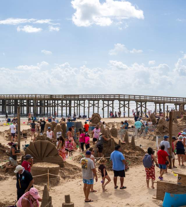 People walking around multiple sand sculptures on the beach during the sandcastle days festival.